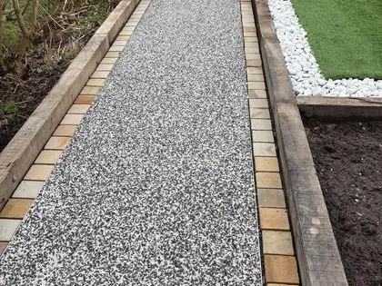 Grey resin bound garden path with brick edging beside an artificial lawn